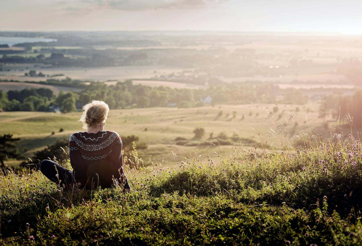 Kvinde sidder på et bakkedrag med udsigt over flot landskab