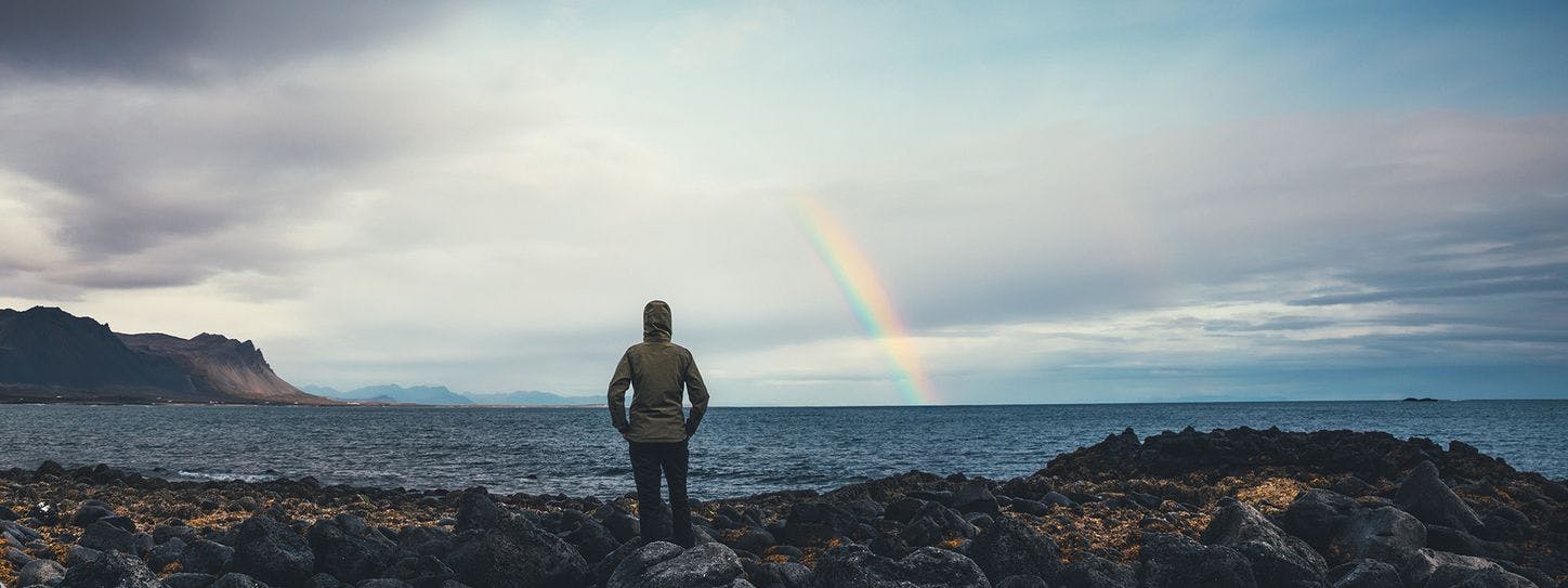 Mand ser udover vandet med regnbue i horisonten