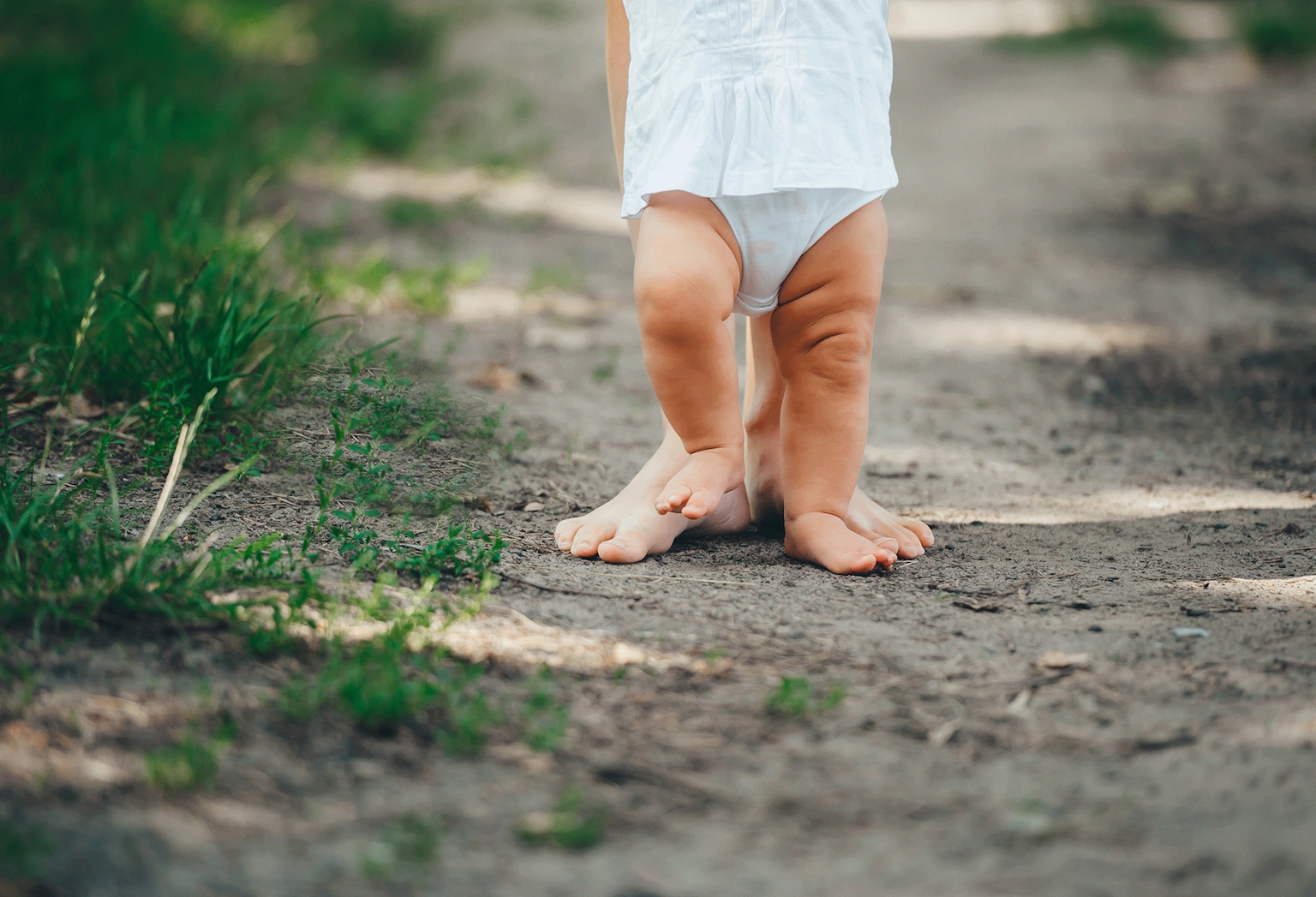 Close-up på benene til en forælder og baby, der går med bare ben i naturen
