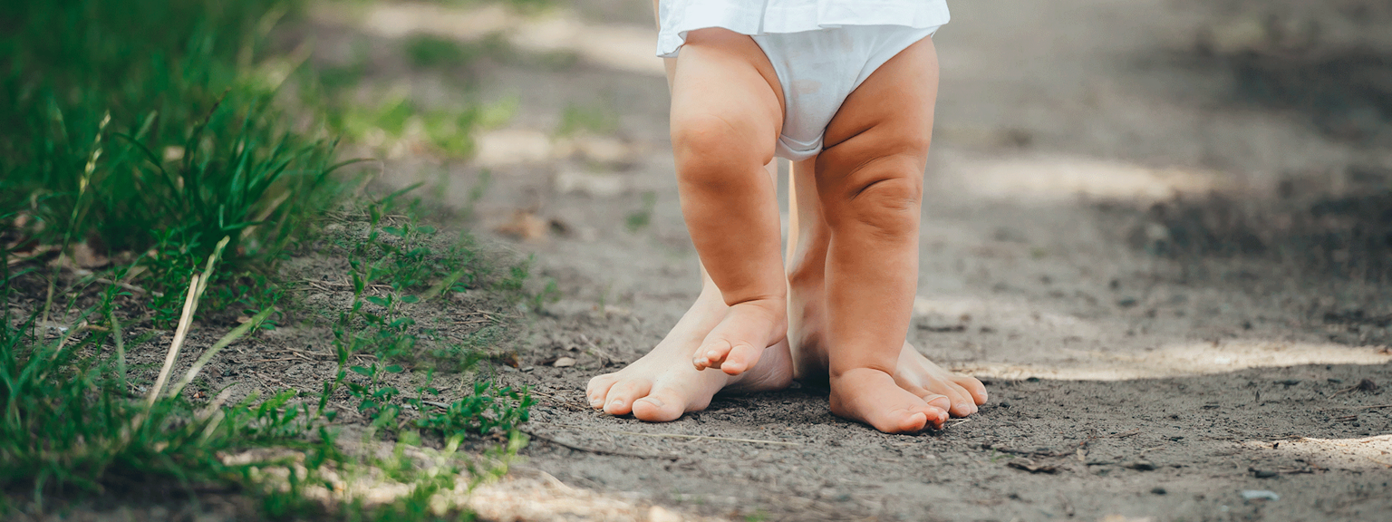 Close-up på benene til en forælder og baby, der går med bare ben i naturen