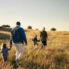 Familie på udflugt henover en mark i flot sollys og havet i horisonten